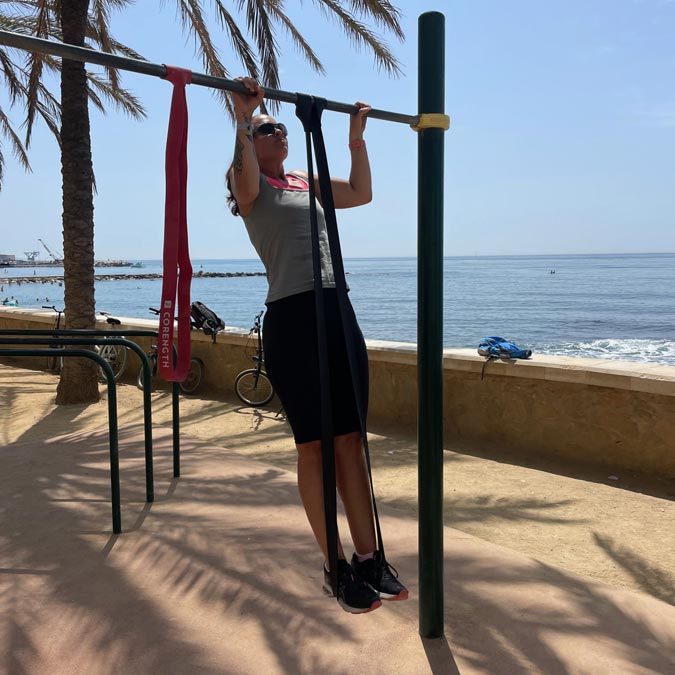 Fitnessurlaub in Marbella mit und von Frank Wierigs mit inseltrainer.com - Das Bild zeigt eine junge Frau, welche Fitness in ihrem Urlaub macht, an einer Klimmzugstange.