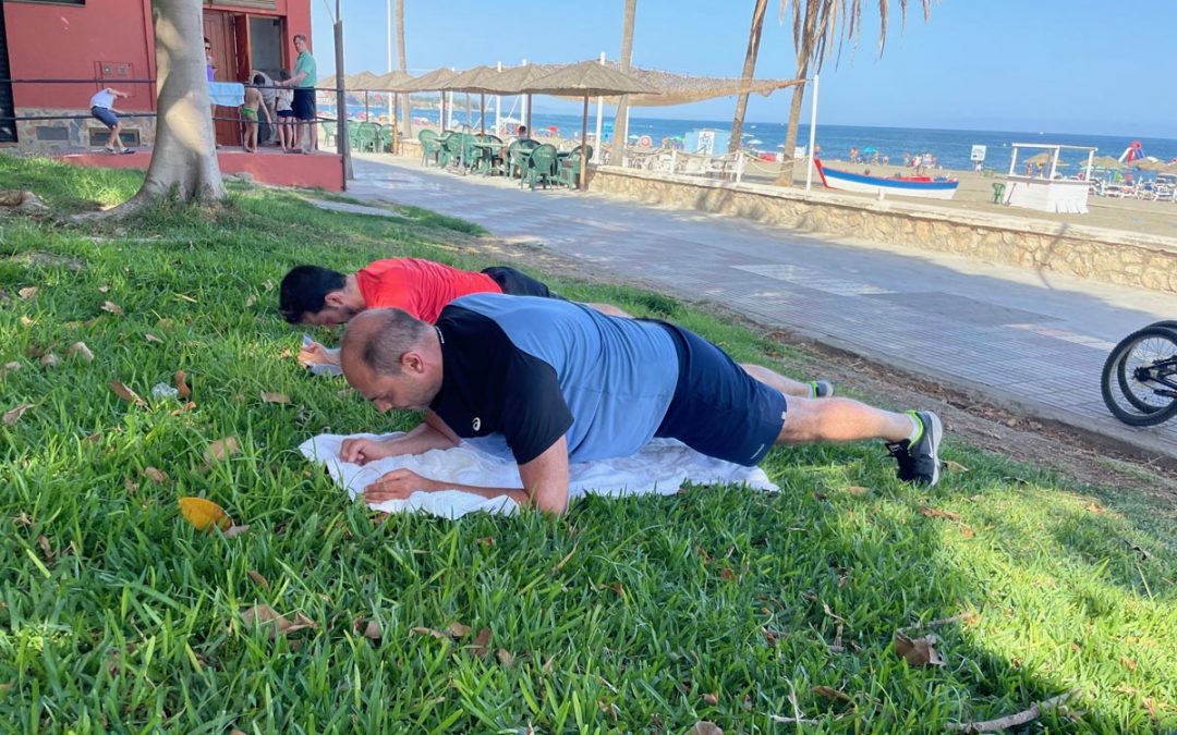 Fitnessurlaub in Marbella mit und von Frank Wierigs mit inseltrainer.com - Das Bild zeigt zwei Männer auf einer grünen Wiese, welche Fitness im Urlaub auf Marbella machen. Im Hintergrund ist der Strand und das Meer zu sehen.